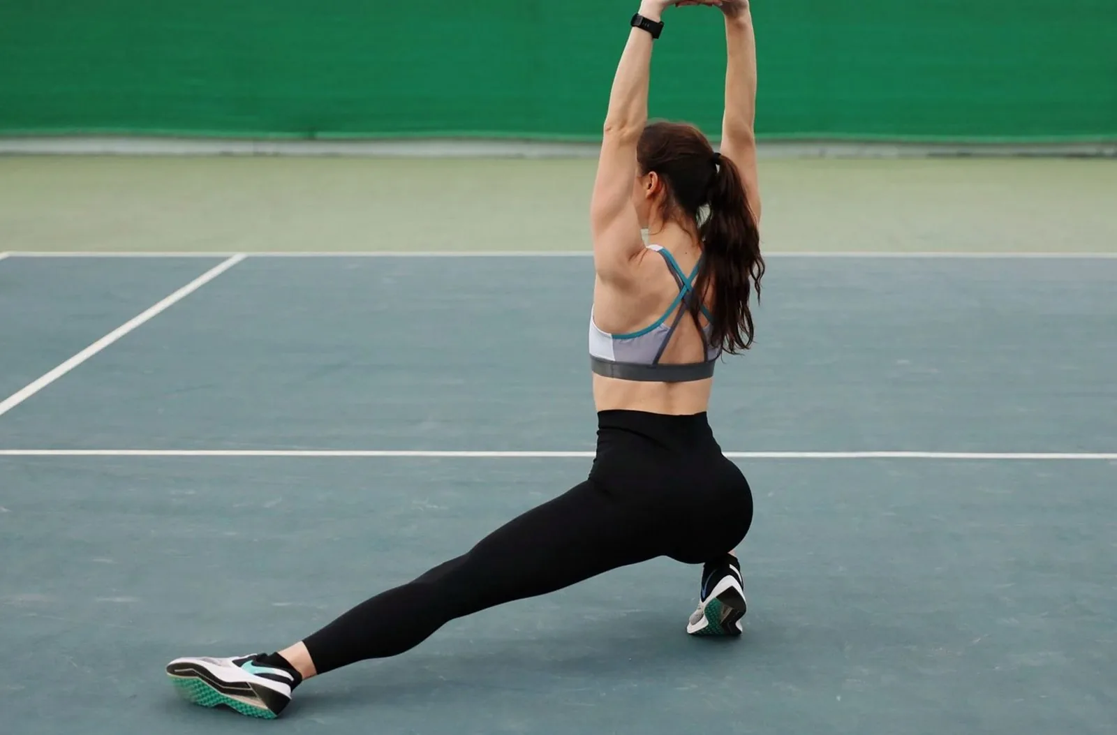 Woman in activewear stretching on a tennis court, promoting a healthy lifestyle.